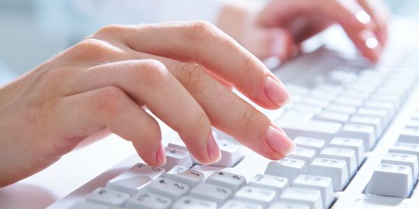 Female hands typing on a white computer keyboard.
